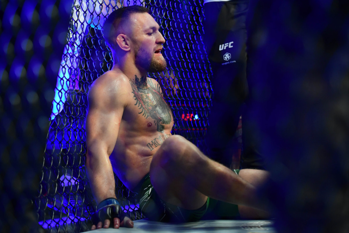 Conor McGregor sits down inside the UFC Octagon after suffering an injury.
